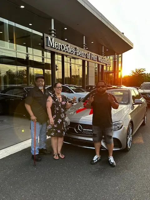 A man and a woman are standing in front of a mercedes benz dealership.