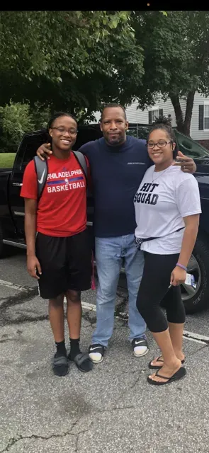 A man and two women are posing for a picture in a parking lot.