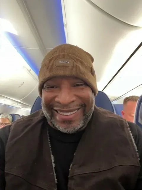 A man wearing a beanie is smiling on an airplane