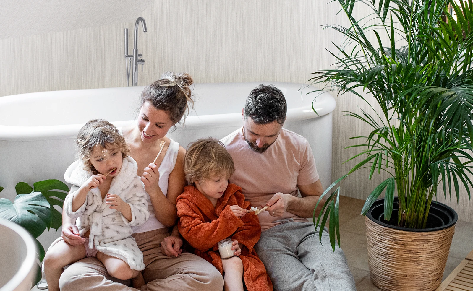 A family is sitting on the floor in a bathroom brushing their teeth.