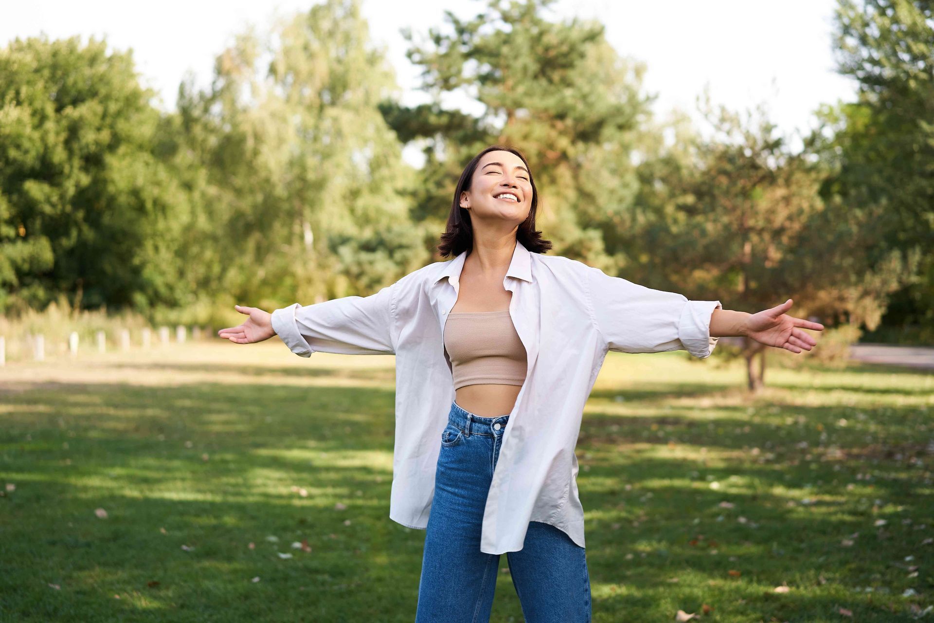 a woman is standing in a park with her arms outstretched