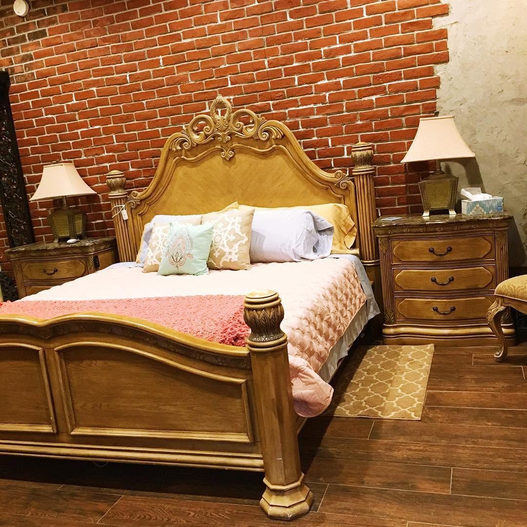 Ornate wooden bed with pink bedding in a rustic bedroom with brick and plaster walls