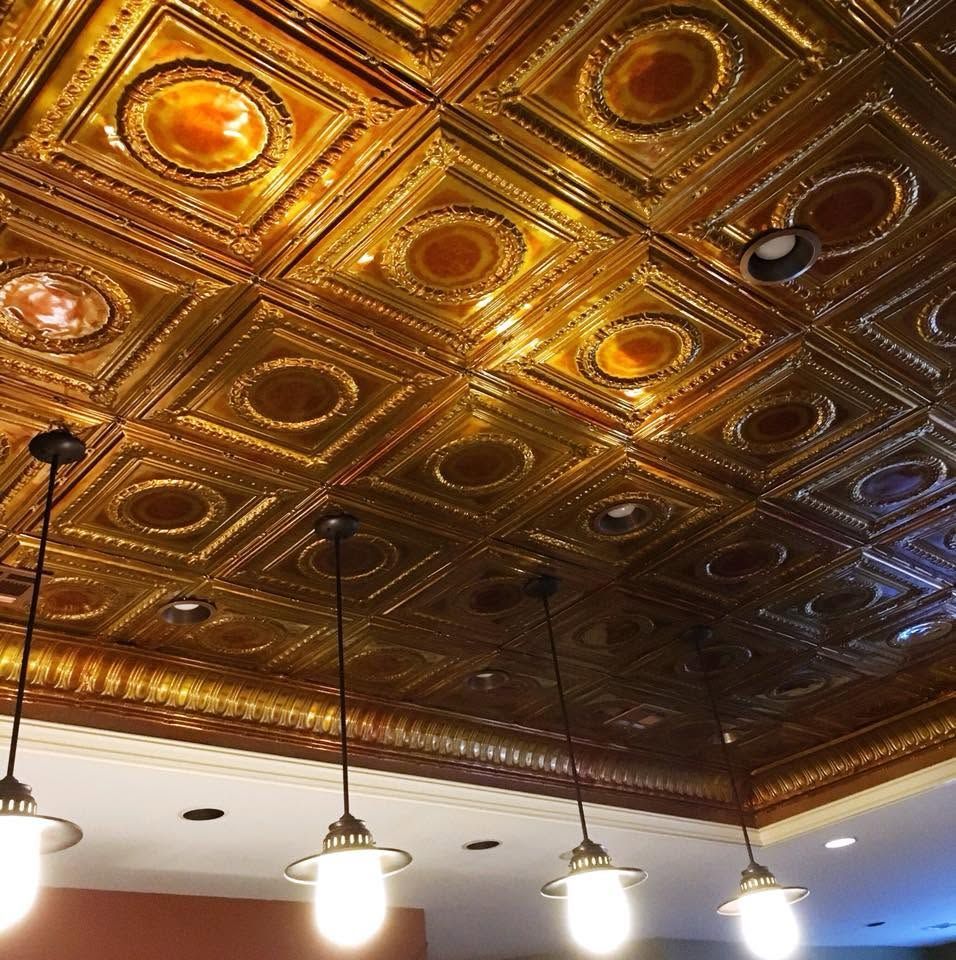 Ornate gold tin ceiling with glowing amber medallions above hanging pendant lights