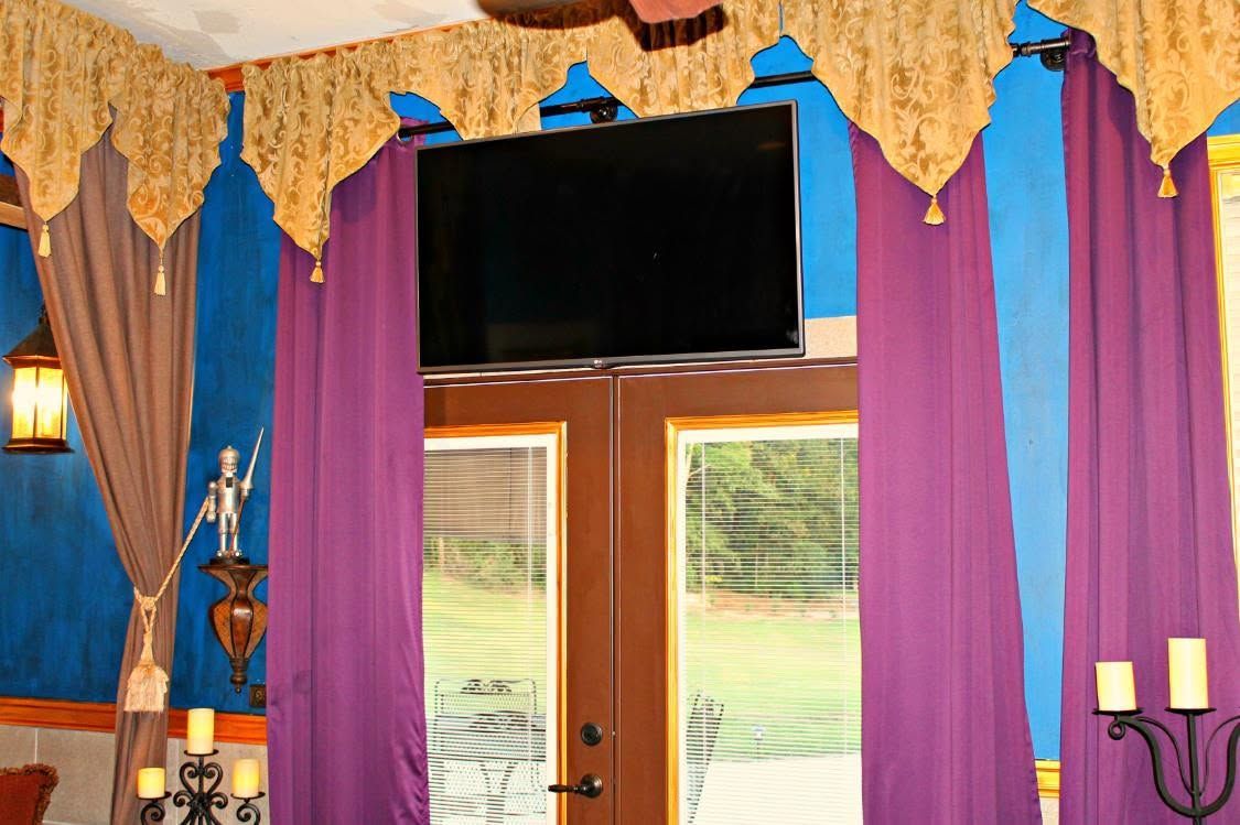 Colorful interior with purple curtains, a large window, and a black TV mounted above the window.