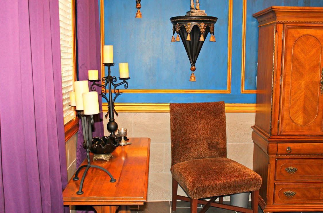 Blue-walled room with brown chair, wooden desk, purple curtain, and ornate hanging lanterns