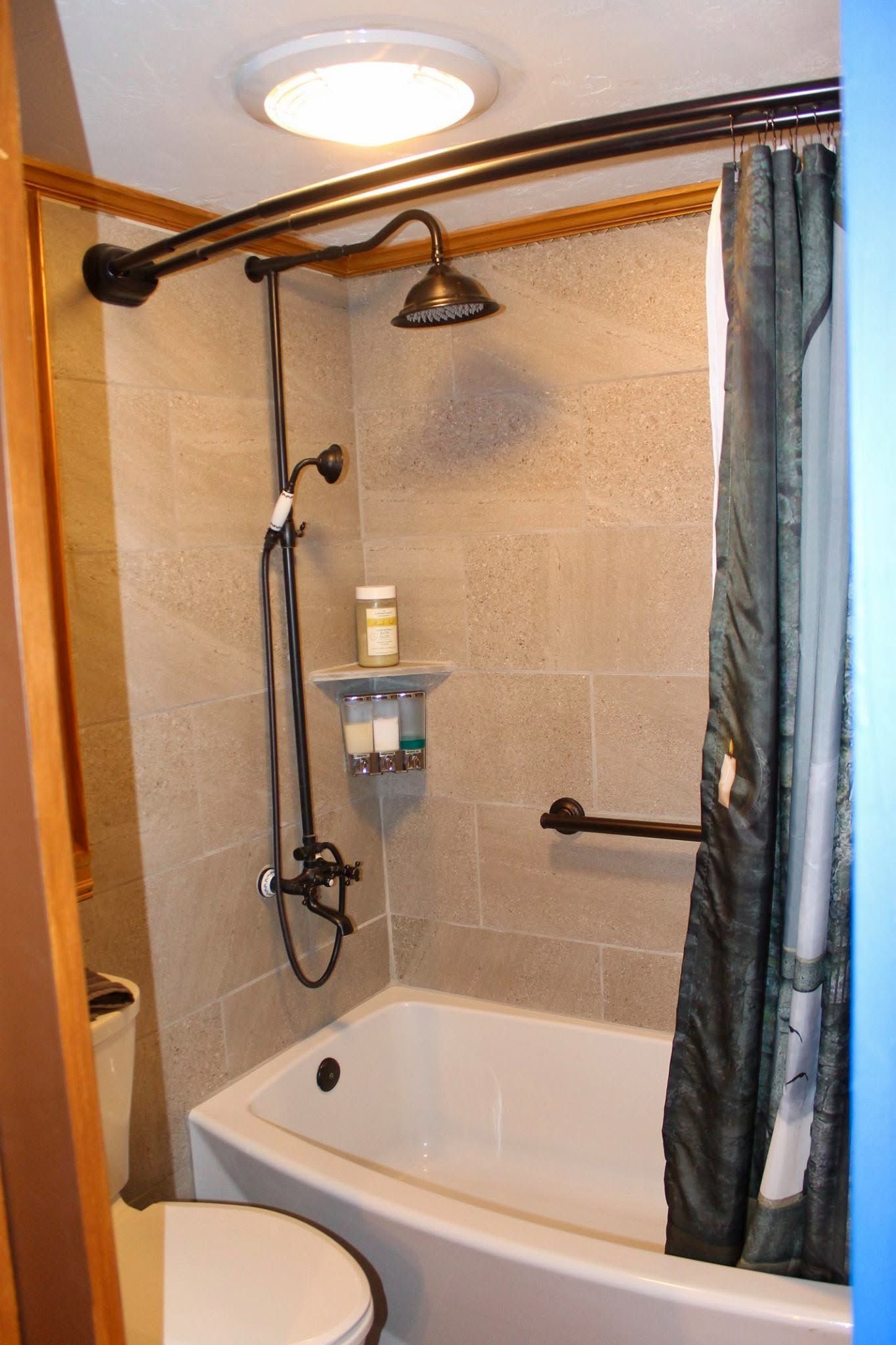 Small bathroom with a shower-tub, curtain, grab bar, and wall-mounted showerhead.