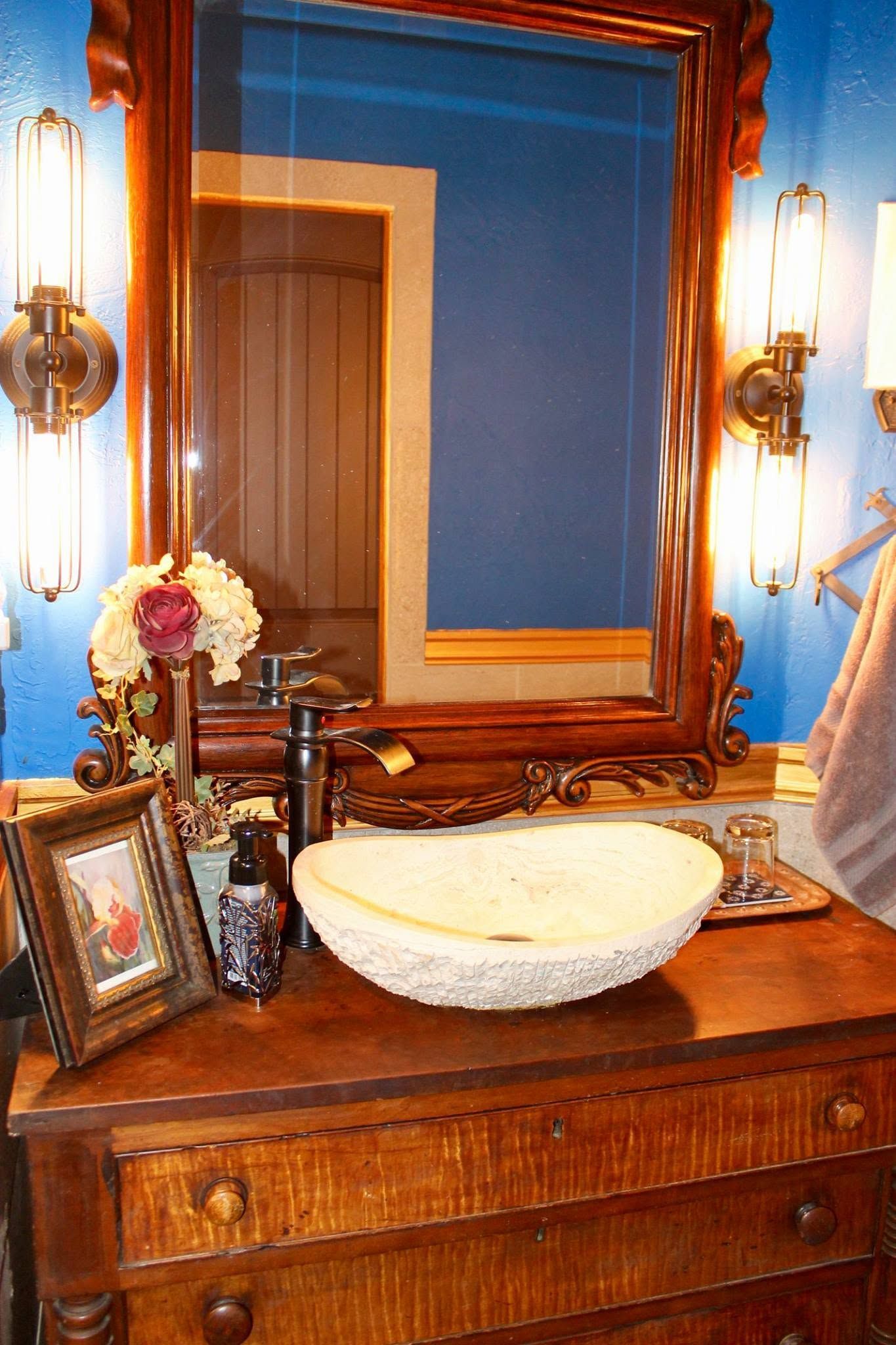 Bathroom vanity with wooden dresser, oval sink, large mirror, and brass wall sconces.