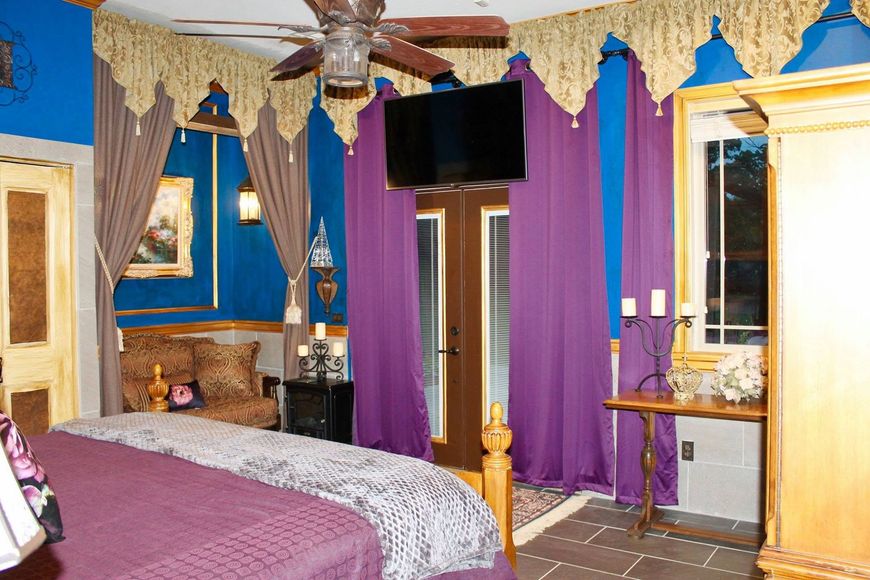 Bedroom with purple drapes, blue walls, a canopy bed, and a ceiling fan-mounted TV.