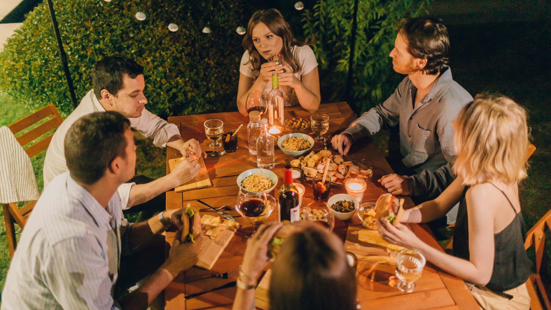 Friends sharing a meal at an outdoor dinner table lit by warm lights