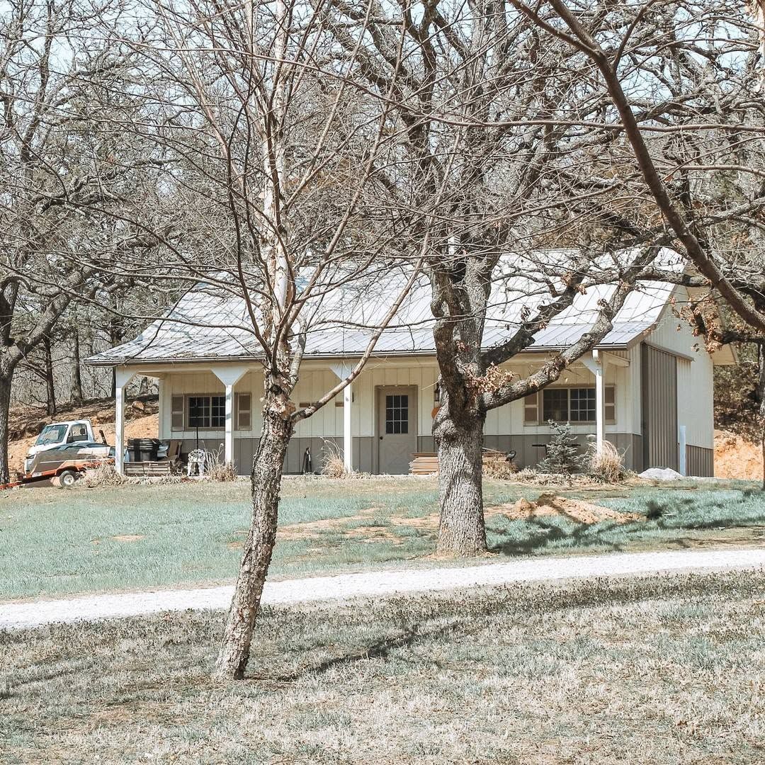 Small beige house with a porch behind leafless trees in a quiet yard