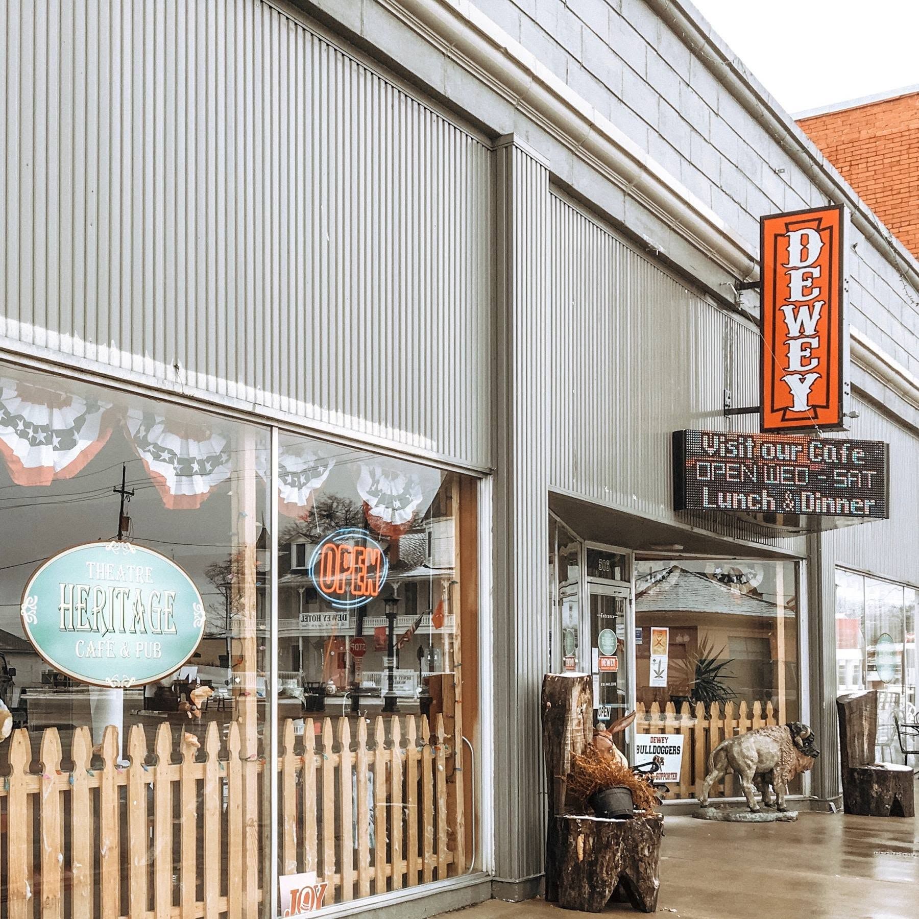 Storefront with large windows, orange sign, and wooden picket fence on a wet street.
