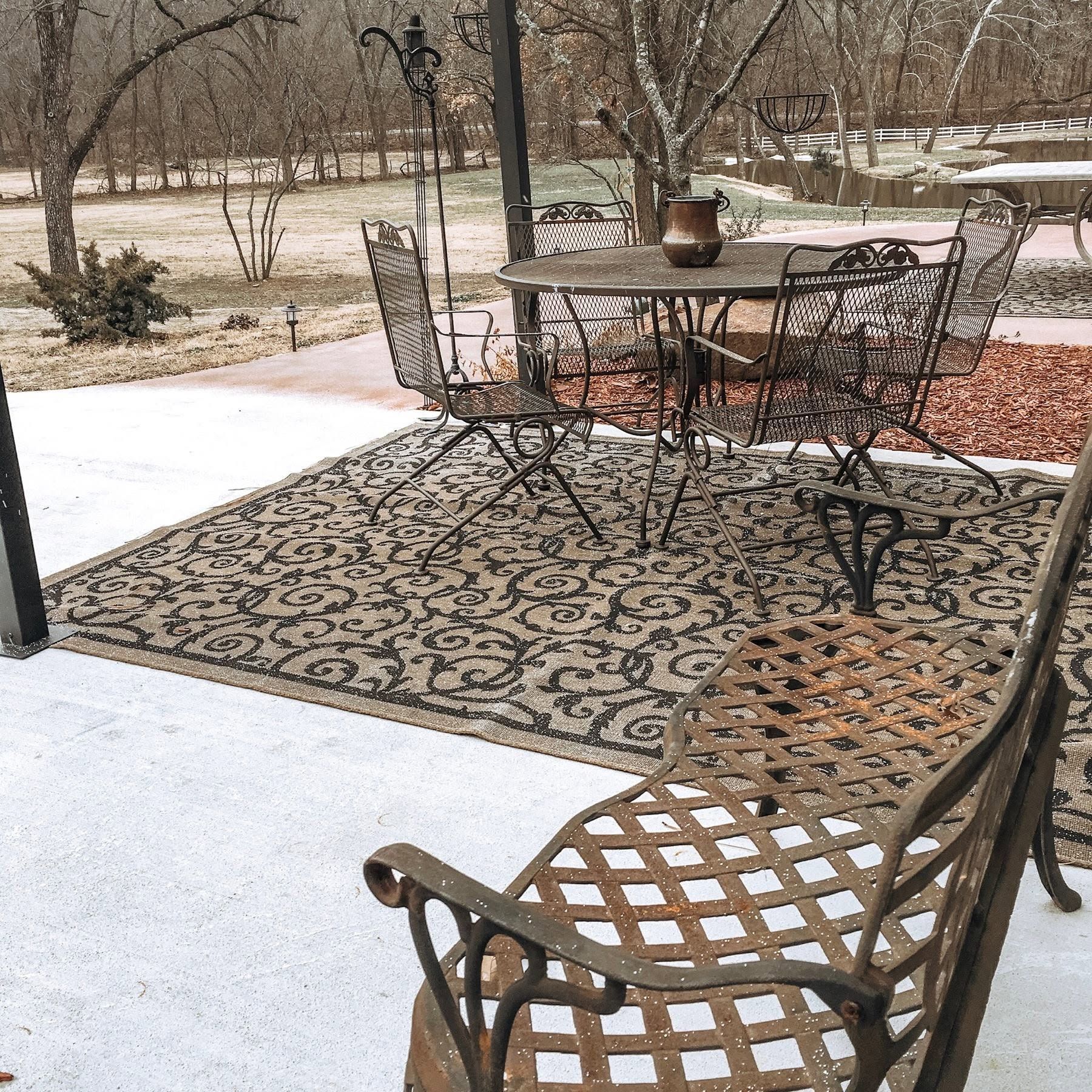 Snowy patio with wrought-iron table and chairs on a patterned outdoor rug