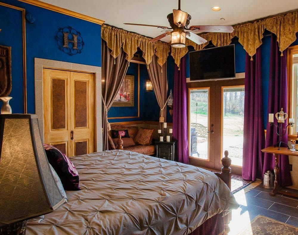 Elegant blue bedroom with purple drapes, a king bed, and sunlight through glass doors