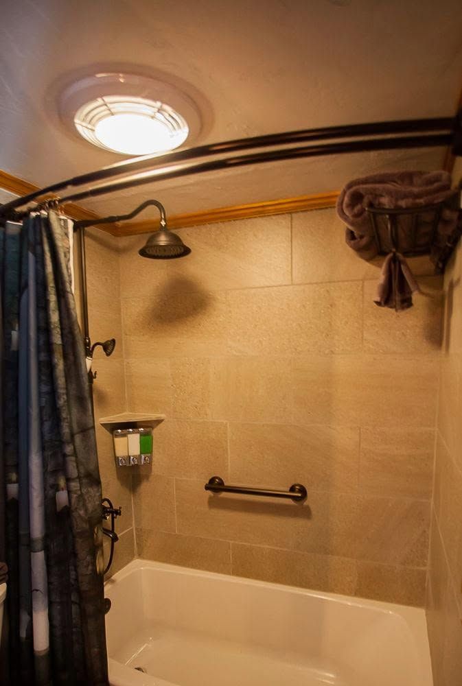 Bathroom shower and bathtub with beige tile, curtain, showerhead, and grab bar