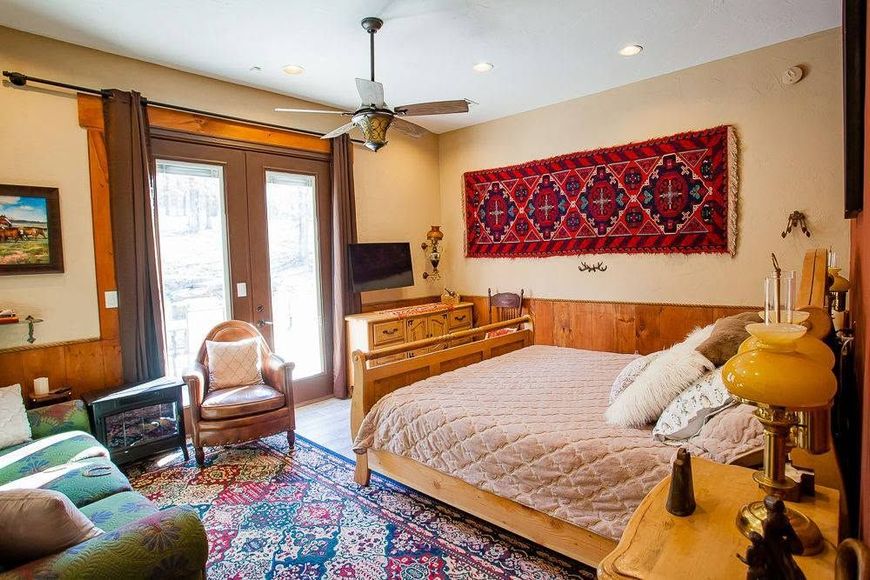 Cozy bedroom with a bed, colorful rug, wood furniture, and French doors opening to a balcony.