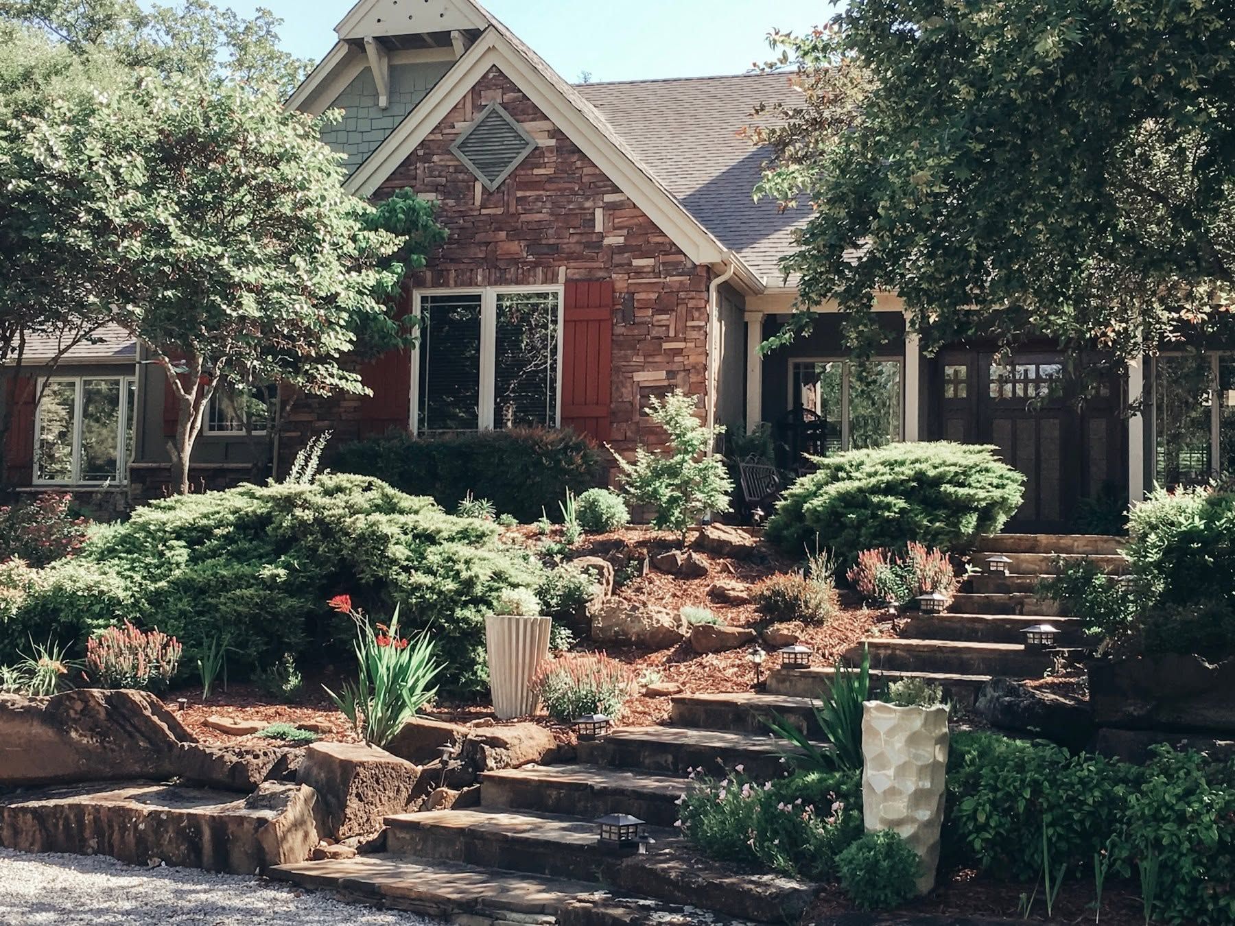 Brick house with a landscaped front yard, stone steps, and trees framing the entrance
