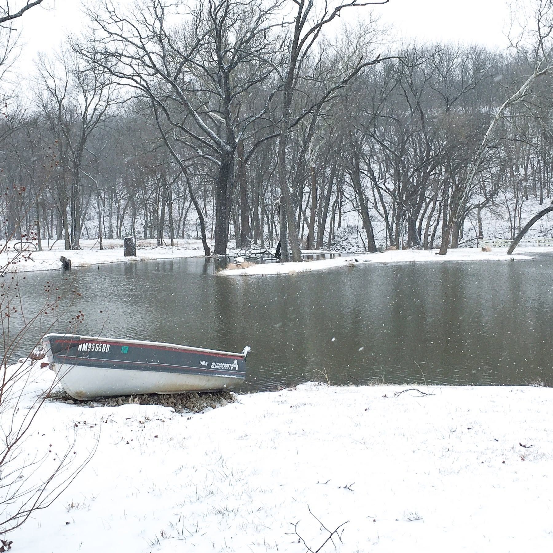 Snowy lakeside with leafless trees and a small boat near the shore
