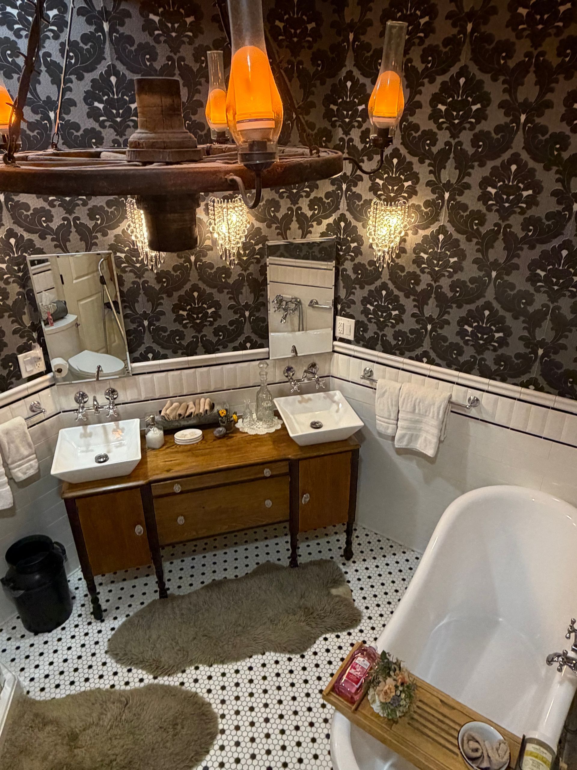 Vintage bathroom with black floral wallpaper, double sink vanity, and a white clawfoot tub.