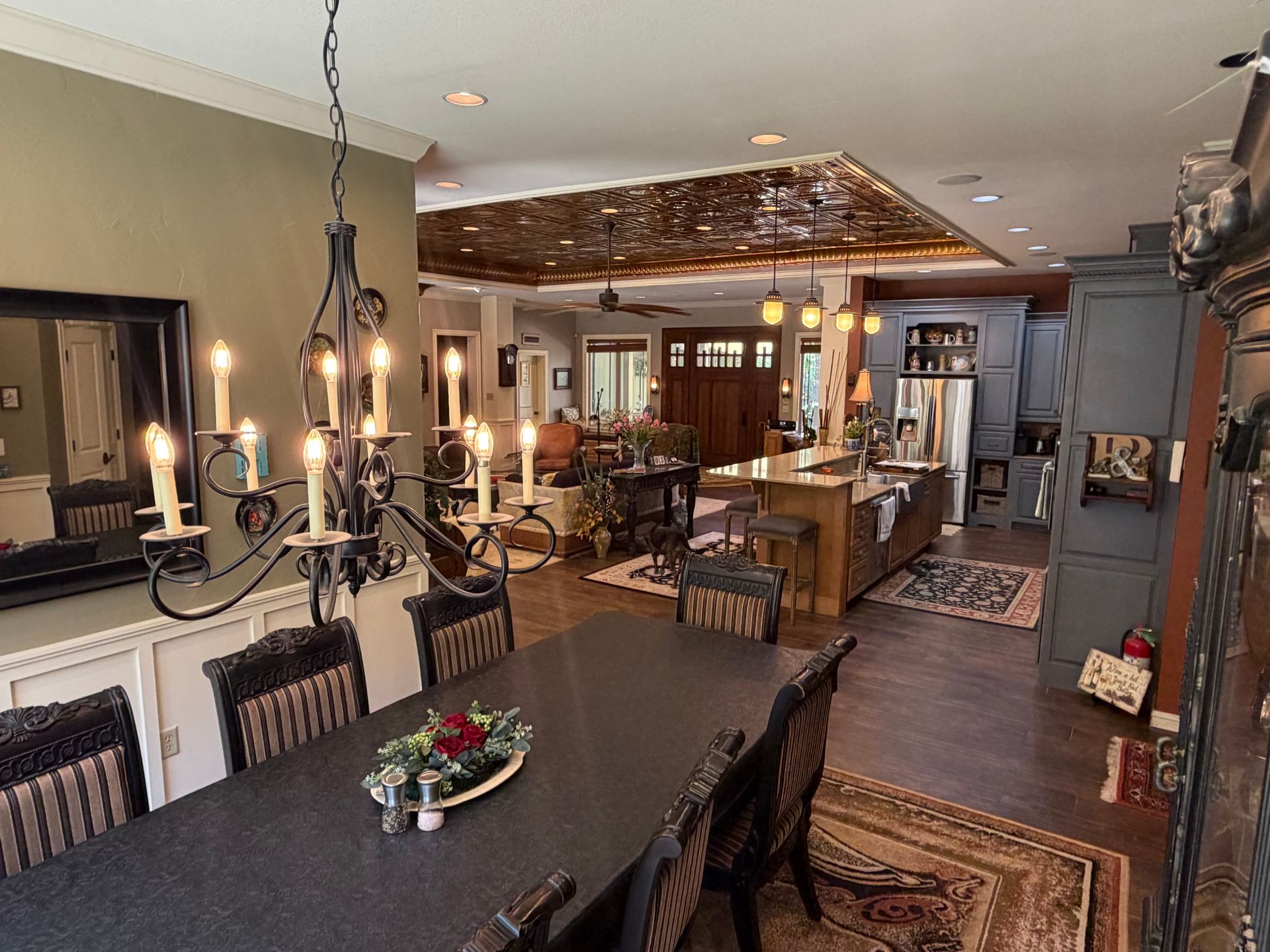 Open-concept kitchen and dining room with dark table, hanging chandeliers, and wood-paneled ceiling