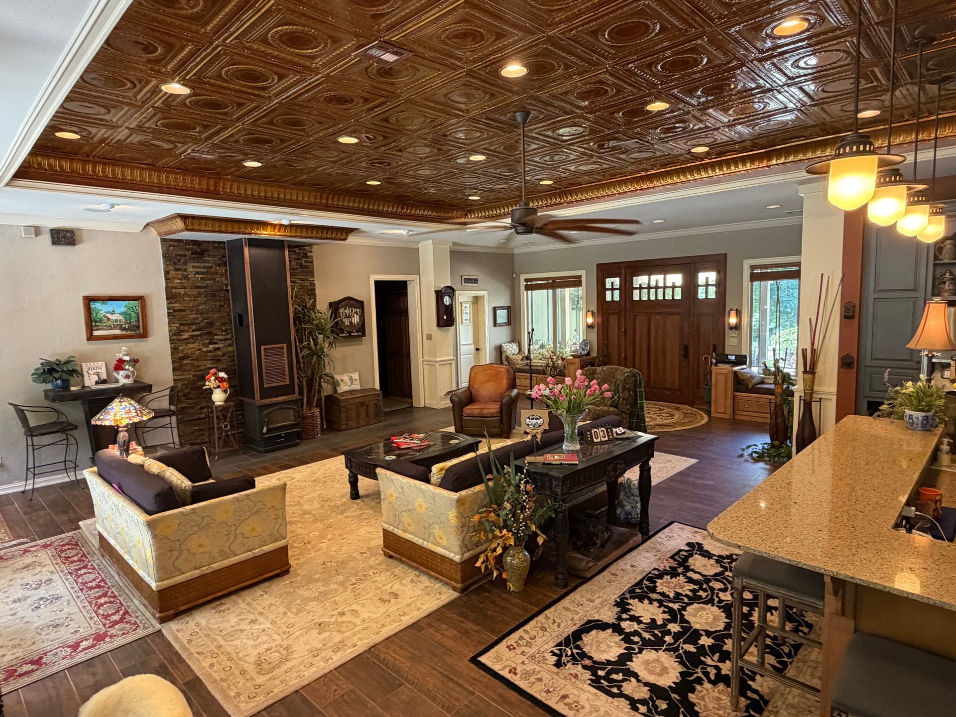 Spacious living room with ornate wood ceiling, sofas, tables, fireplace, and warm lighting