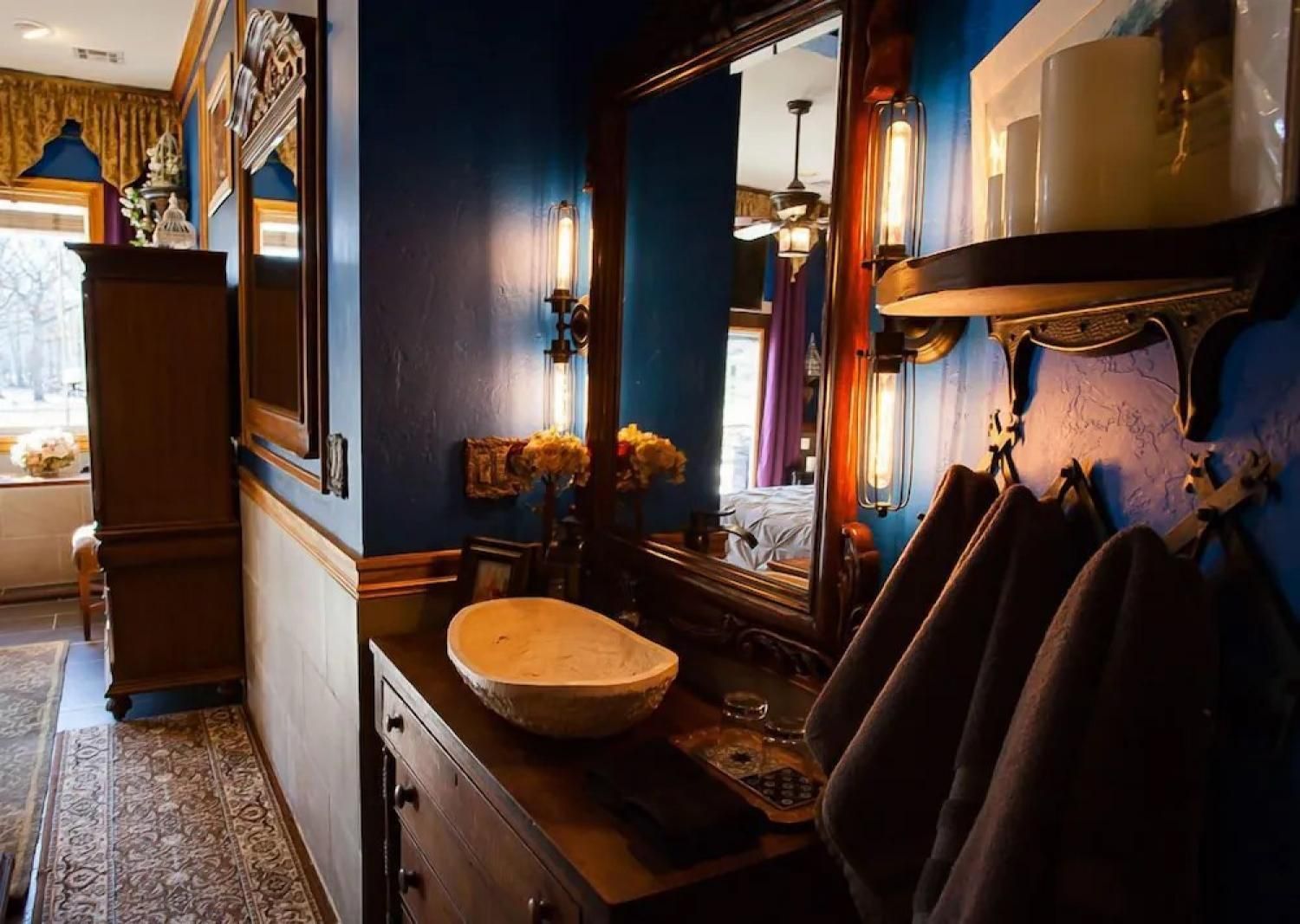 Blue bathroom vanity with ornate mirror, wall sconces, and hanging dark towels