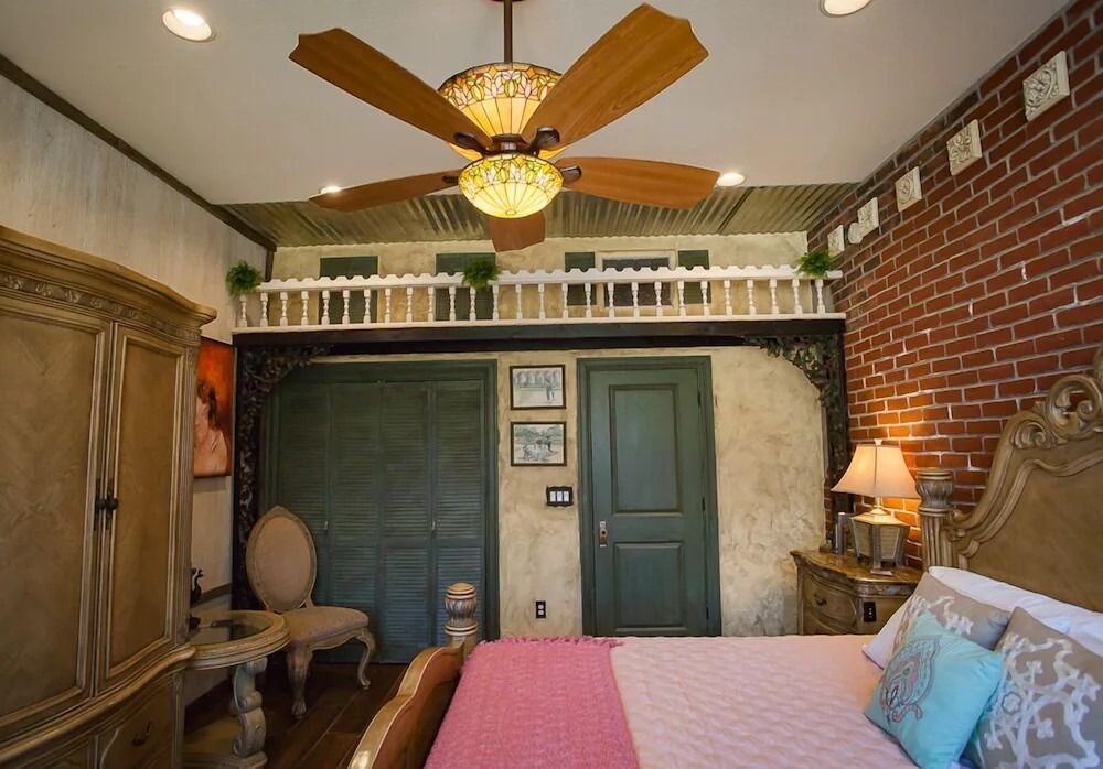 Cozy bedroom with brick accent wall, ceiling fan, vintage furniture, and a bed with pink bedding.