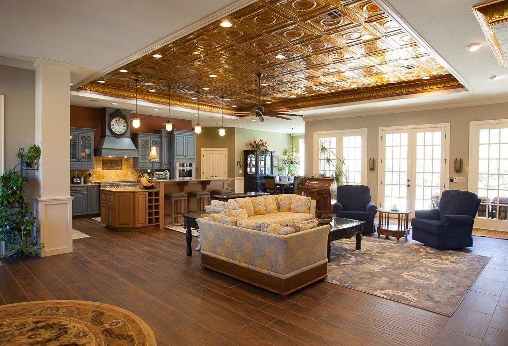 Open-plan living room with wood ceiling, kitchen island, sofa, blue chairs, and French doors.
