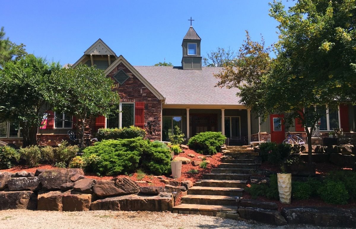 Stone house with a front porch, red shutters, and landscaped garden steps under a clear blue sky
