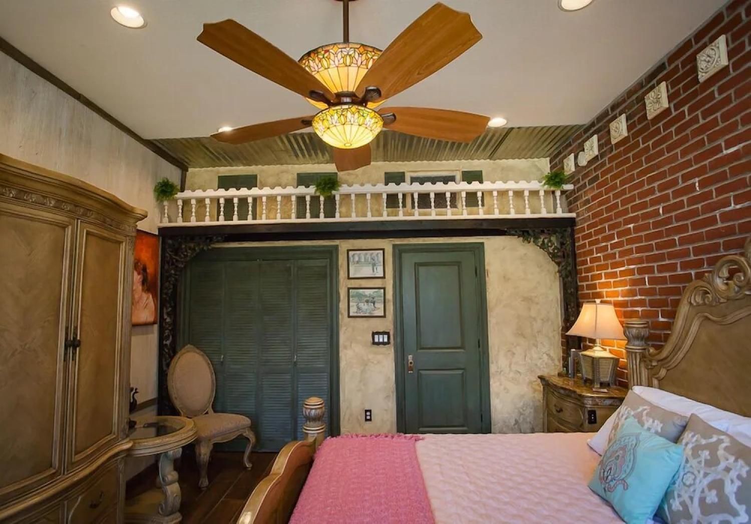 Cozy bedroom with brick wall, green doors, ornate ceiling fan, and upholstered furniture
