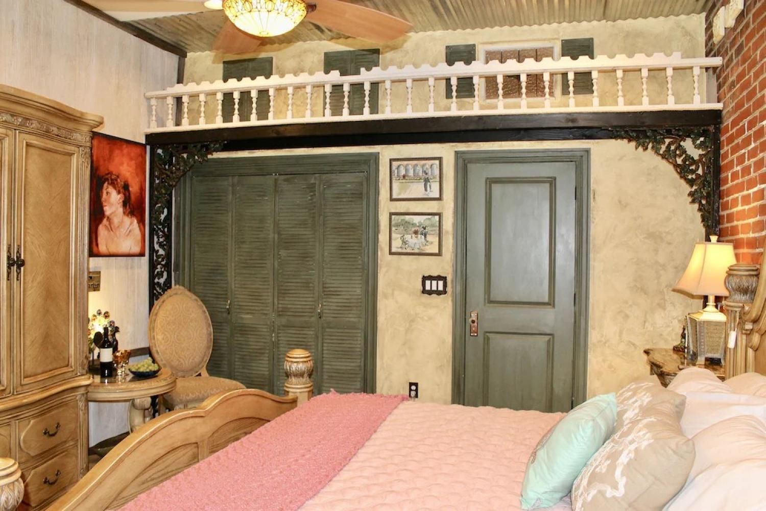 Vintage bedroom with pink bedspread, green closet doors, and lofted shelf above the bed.