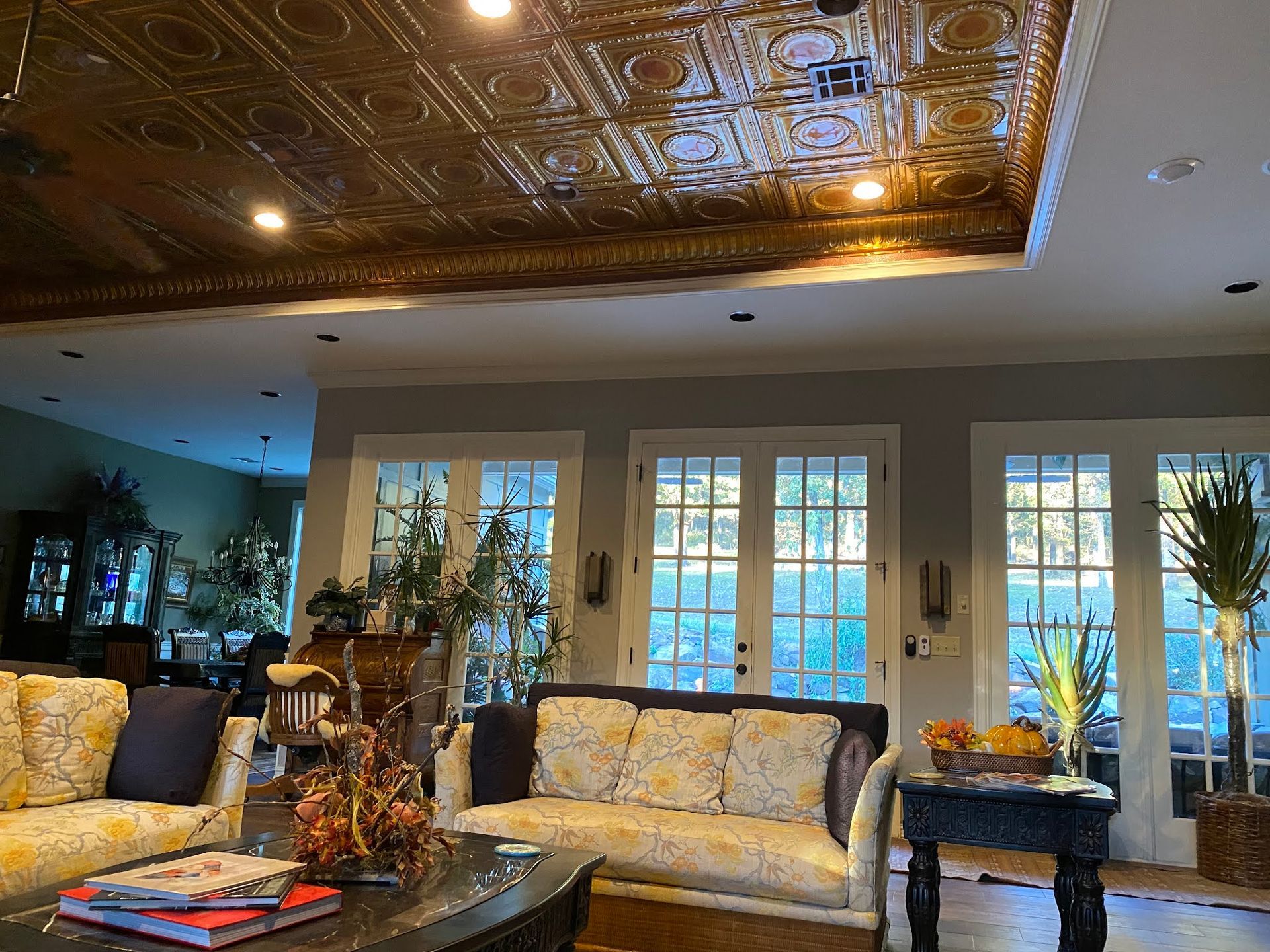 Elegant living room with floral sofas, glass doors, and a decorative tin ceiling