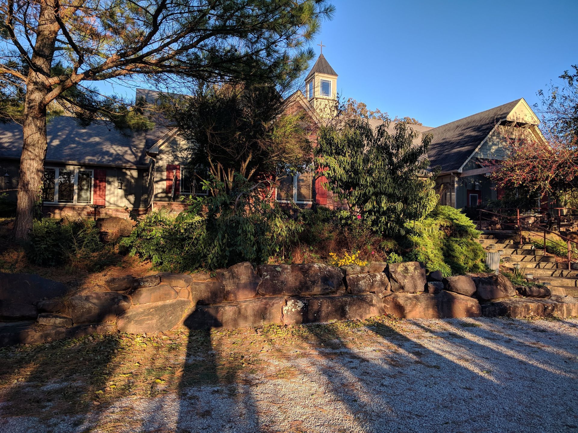 Stone house surrounded by autumn trees and shrubs, with a small tower and long shadows at sunset