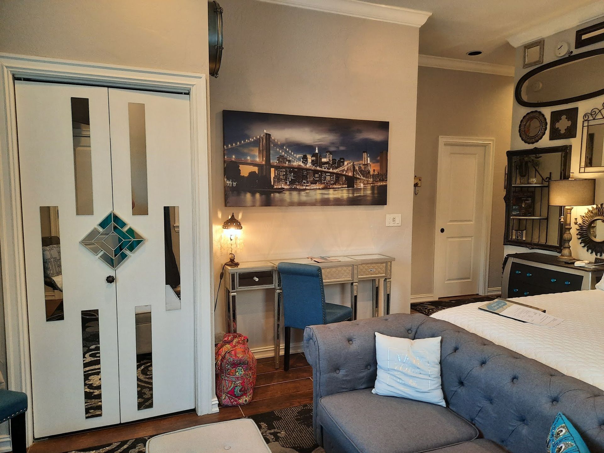 Cozy bedroom with a bed, desk, mirrored closet doors, and a cityscape wall print