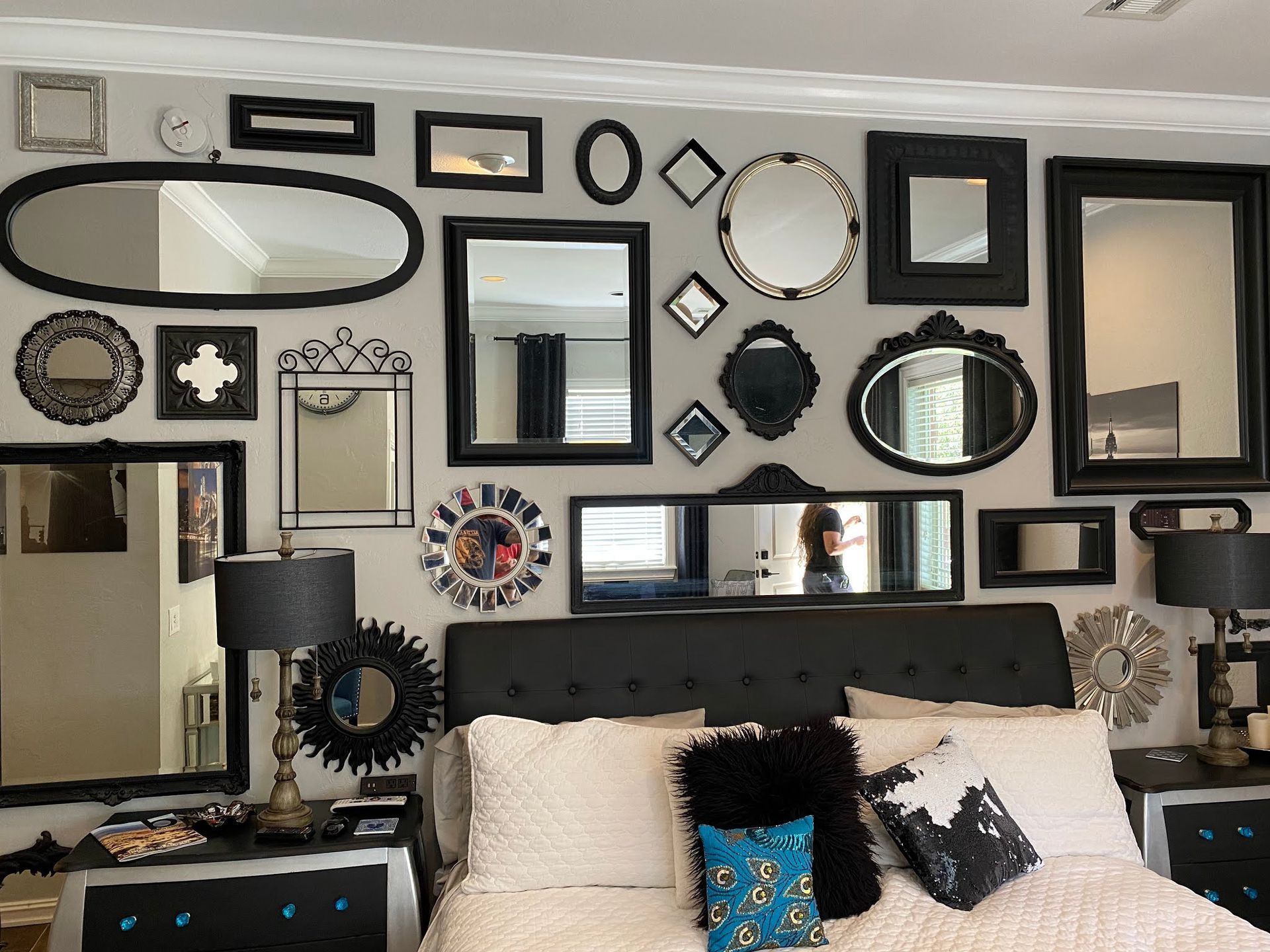 Bedroom wall covered with assorted black-framed mirrors above a bed with pillows