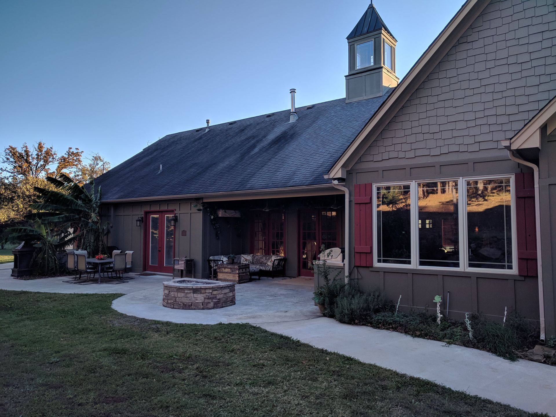 Rustic building with a sloped roof, red doors, and a front patio at dusk