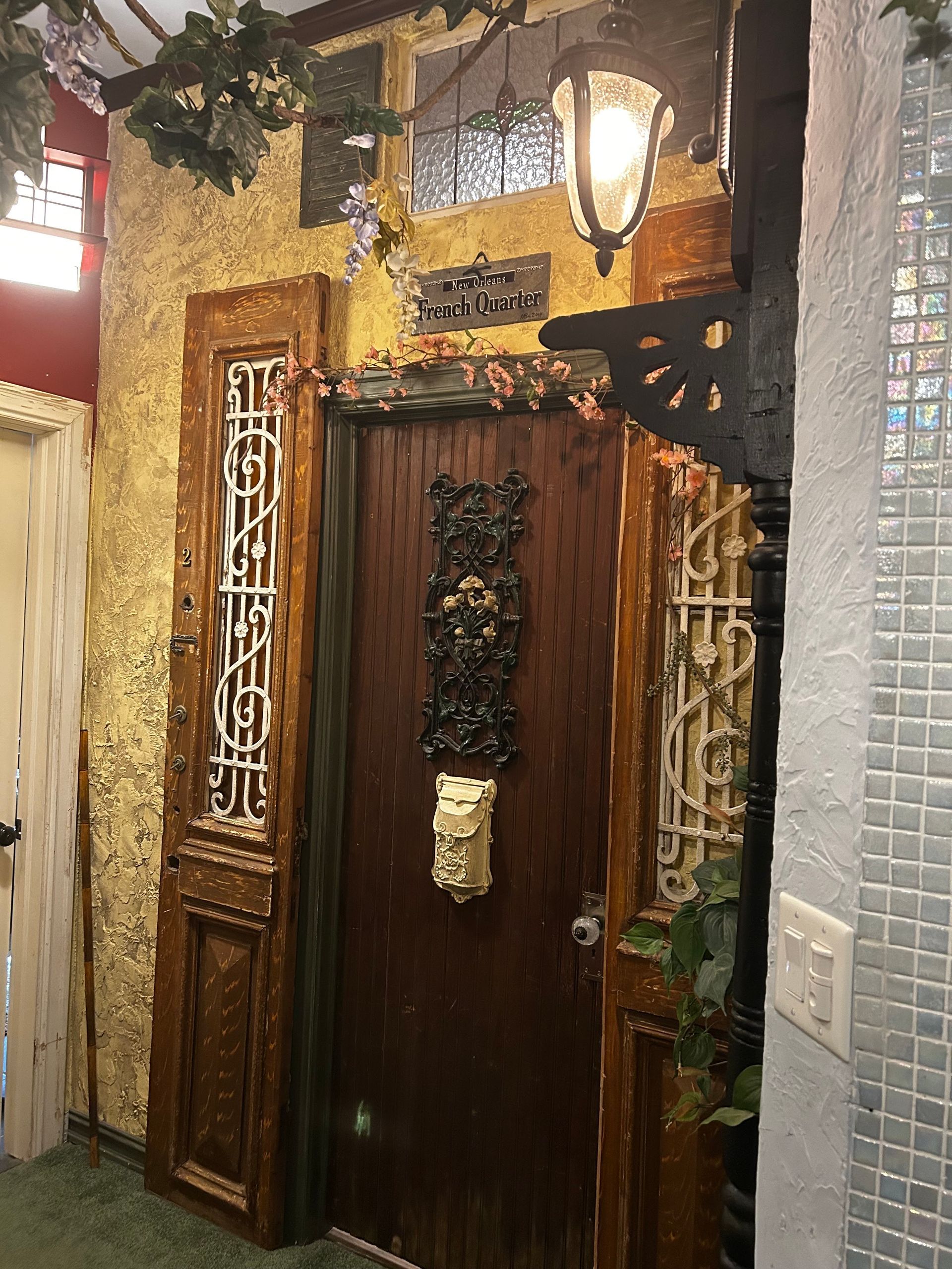 Decorative wooden doorway with mosaic walls, gold lantern, and leafy trim in a narrow entryway