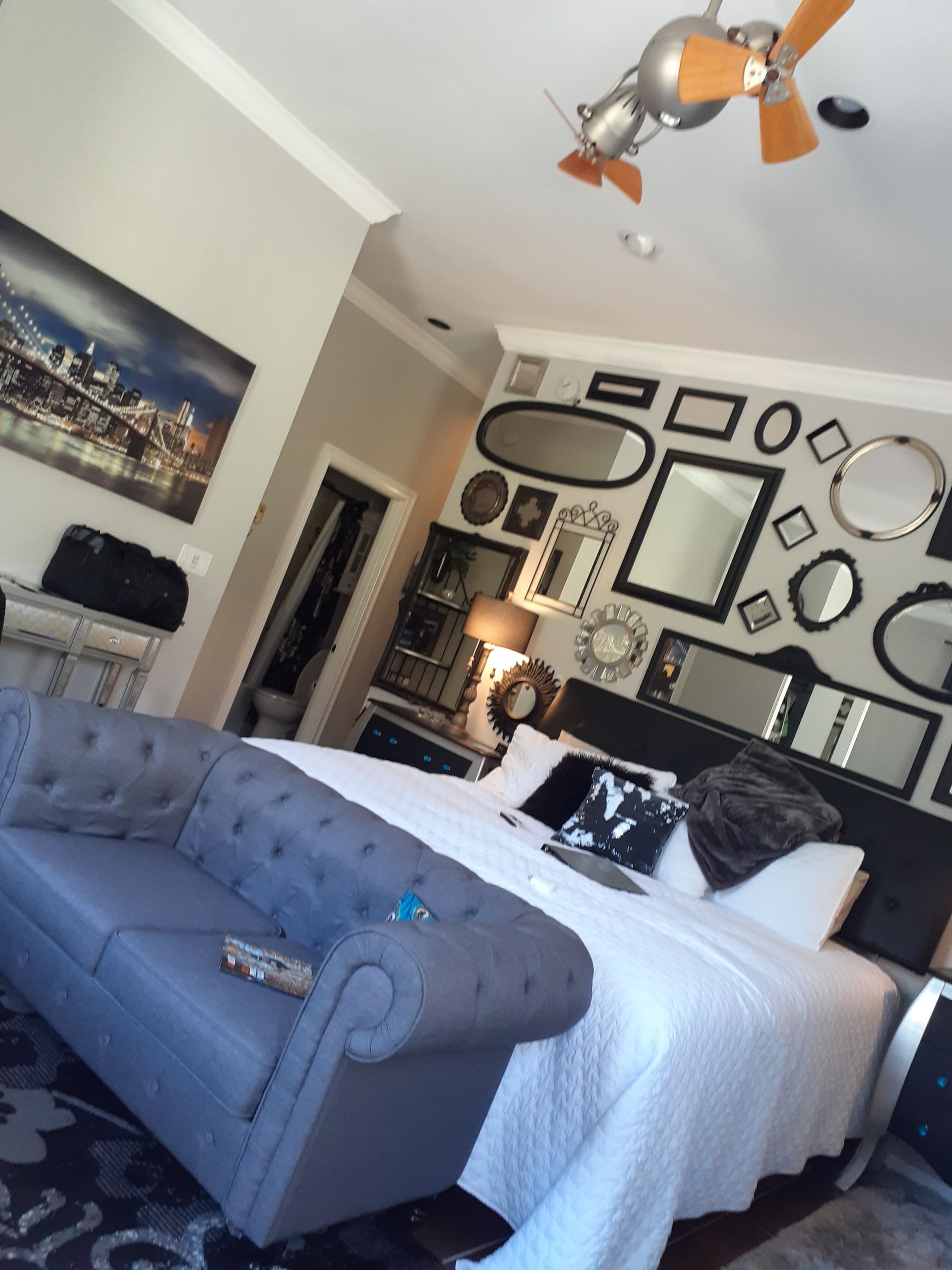 Stylish bedroom with gray tufted sofa, white bed, mirror wall art, and cityscape painting