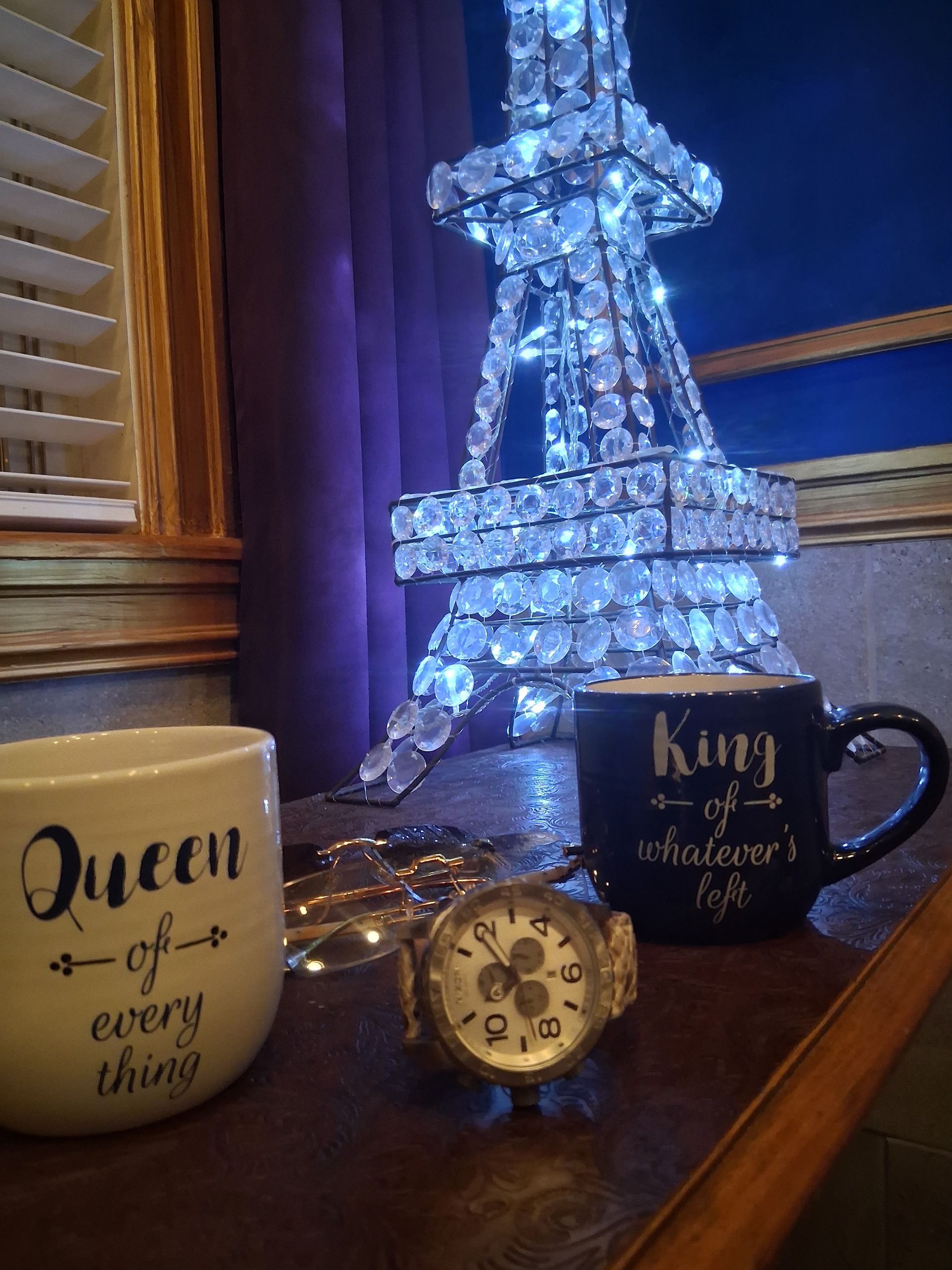 Decorative Eiffel Tower lights beside mugs and a small clock on a wooden shelf