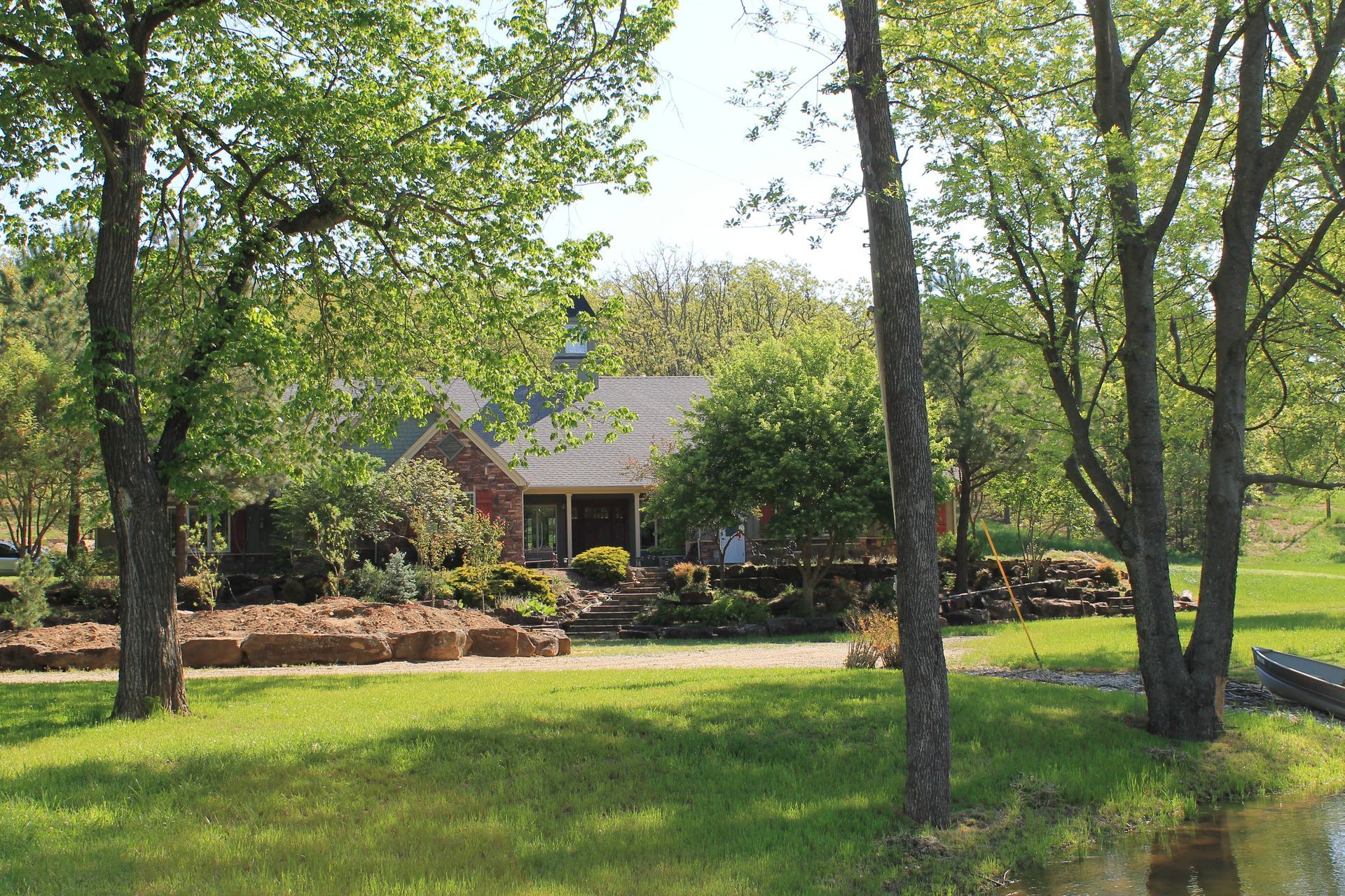 House behind trees in a green yard with a stone border and shrubs