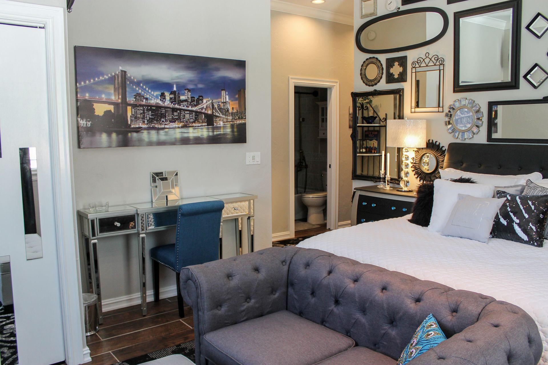 Modern bedroom with tufted gray sofa, desk, wall art, mirror, and cityscape photo above the bed
