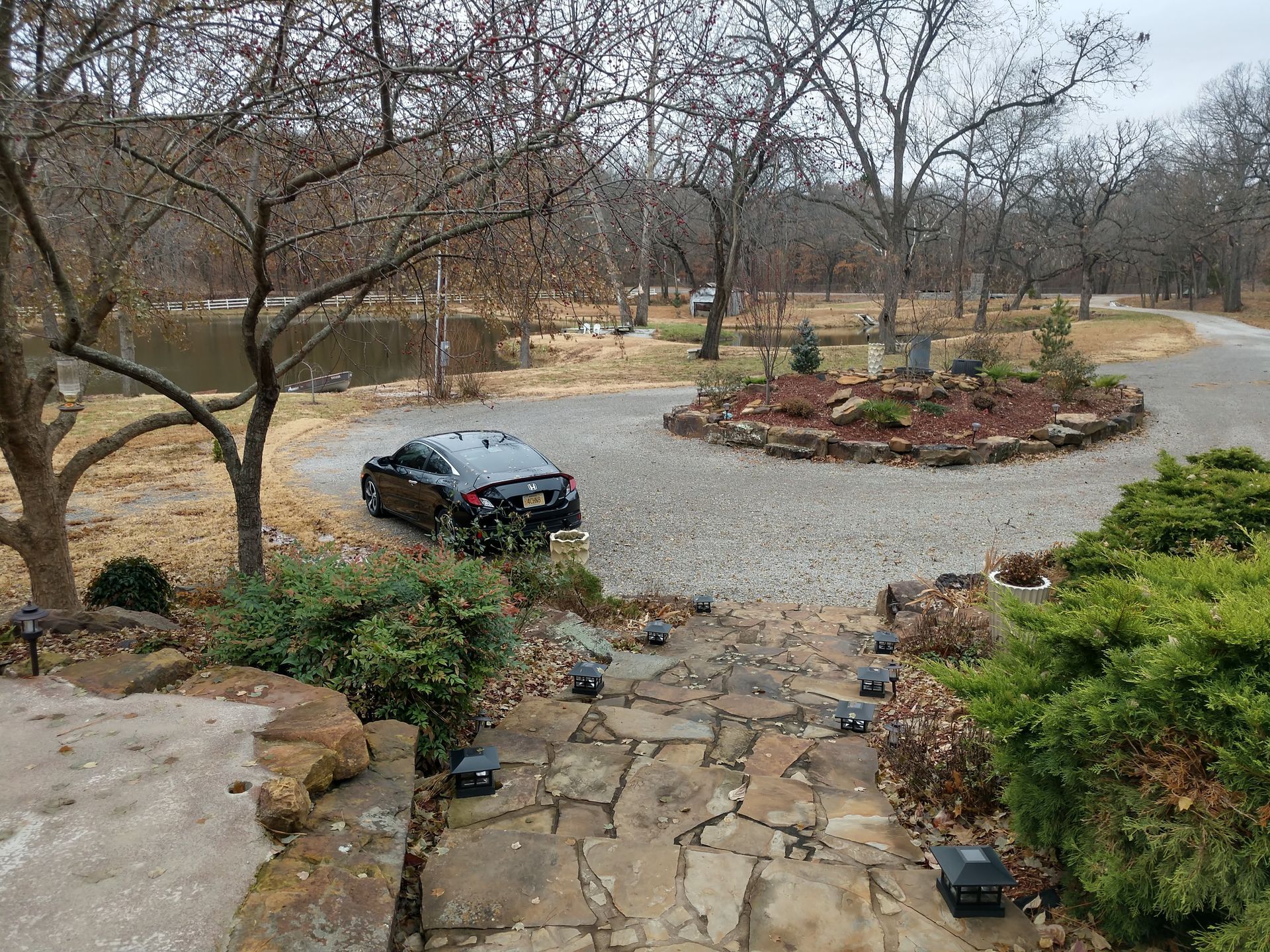 A black SUV on a winding gravel drive in a leafless landscaped garden with stone steps and shrubs
