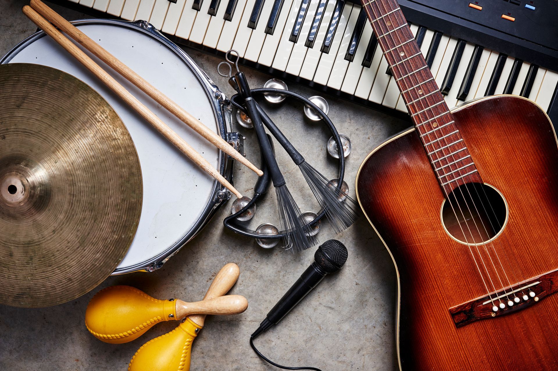 A guitar , drum , keyboard , microphone , tambourine and cymbals are on a table.