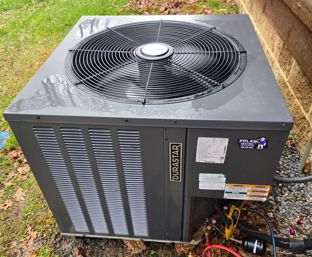 Outdoor air conditioner unit on gravel beside steps, with red and blue hoses attached.