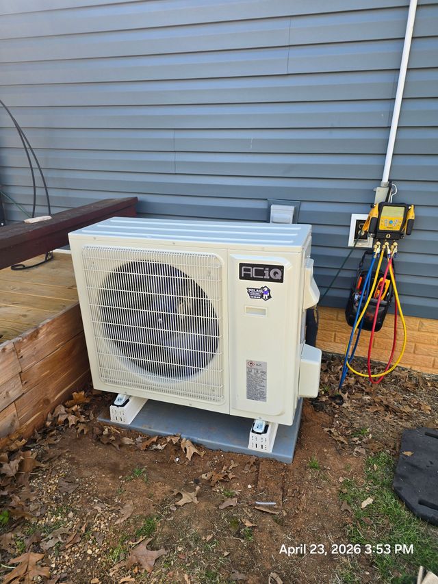 Outdoor HVAC unit on a concrete pad beside a house wall and plants.