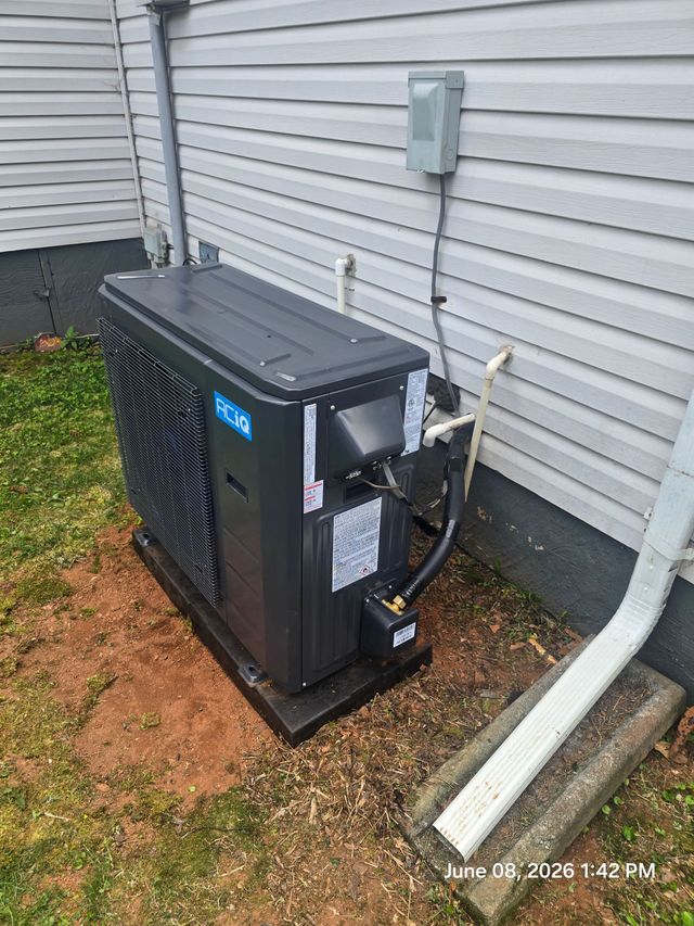 Technician kneeling beside an outdoor HVAC unit, using tools to repair it on a rooftop.