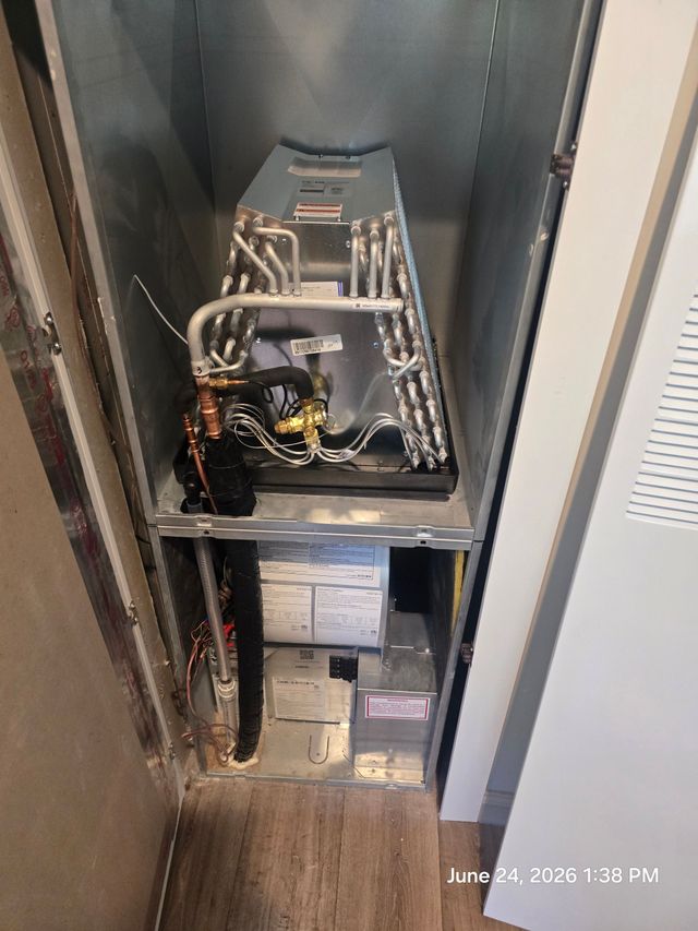 Gray furnace in a hallway closet with exposed ductwork and an open door nearby