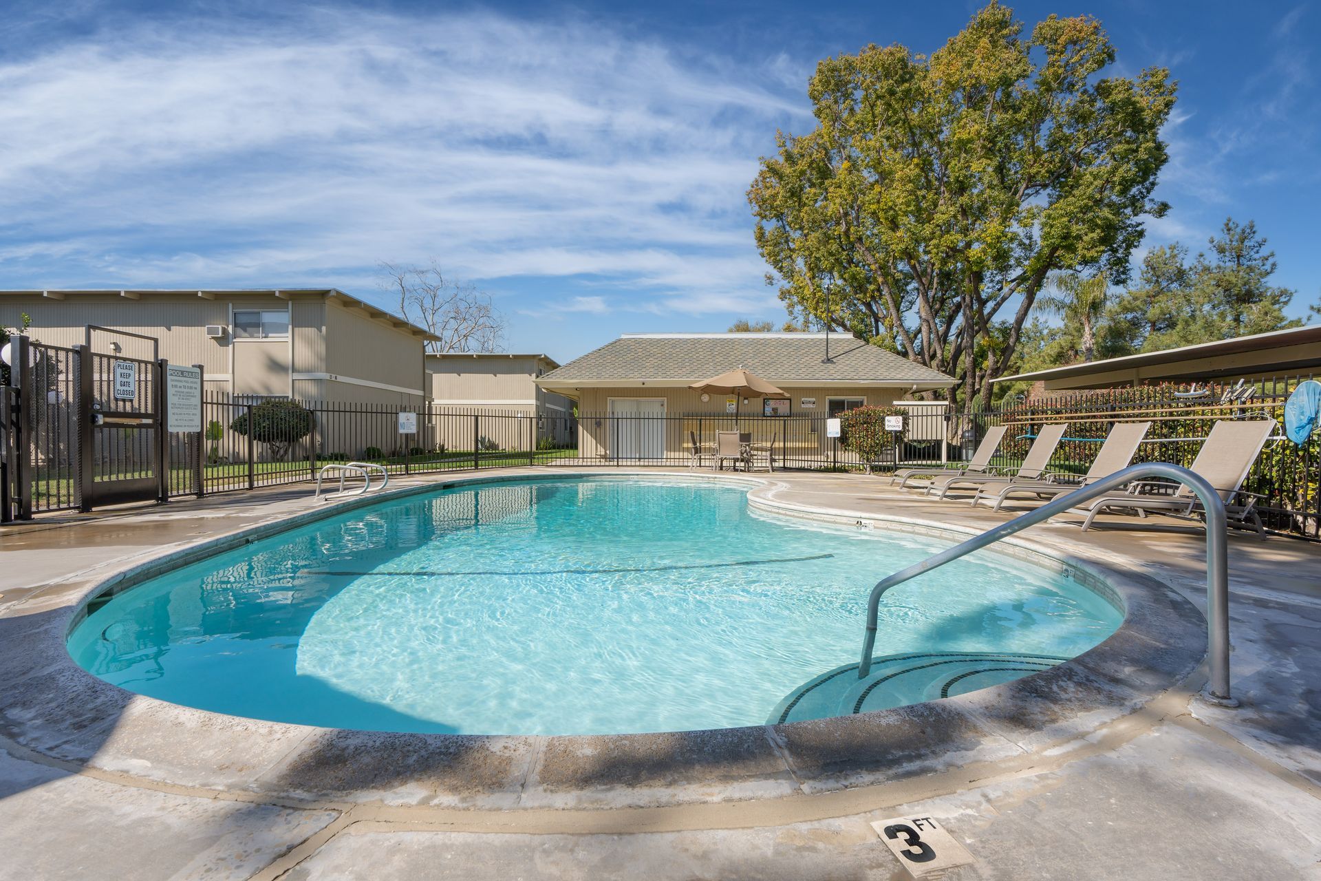 Pool with blue water, lounge chairs, and a small building on a sunny day.