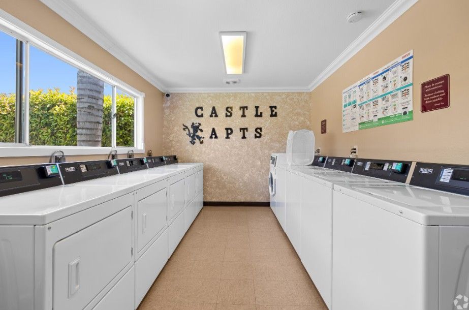 Laundry room with white appliances, sink, clock, and tan walls.