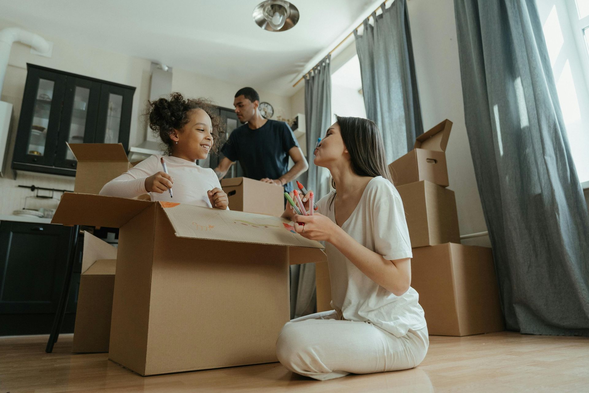 Family unpacking boxes in a kitchen, daughter and mother smiling, father in background.