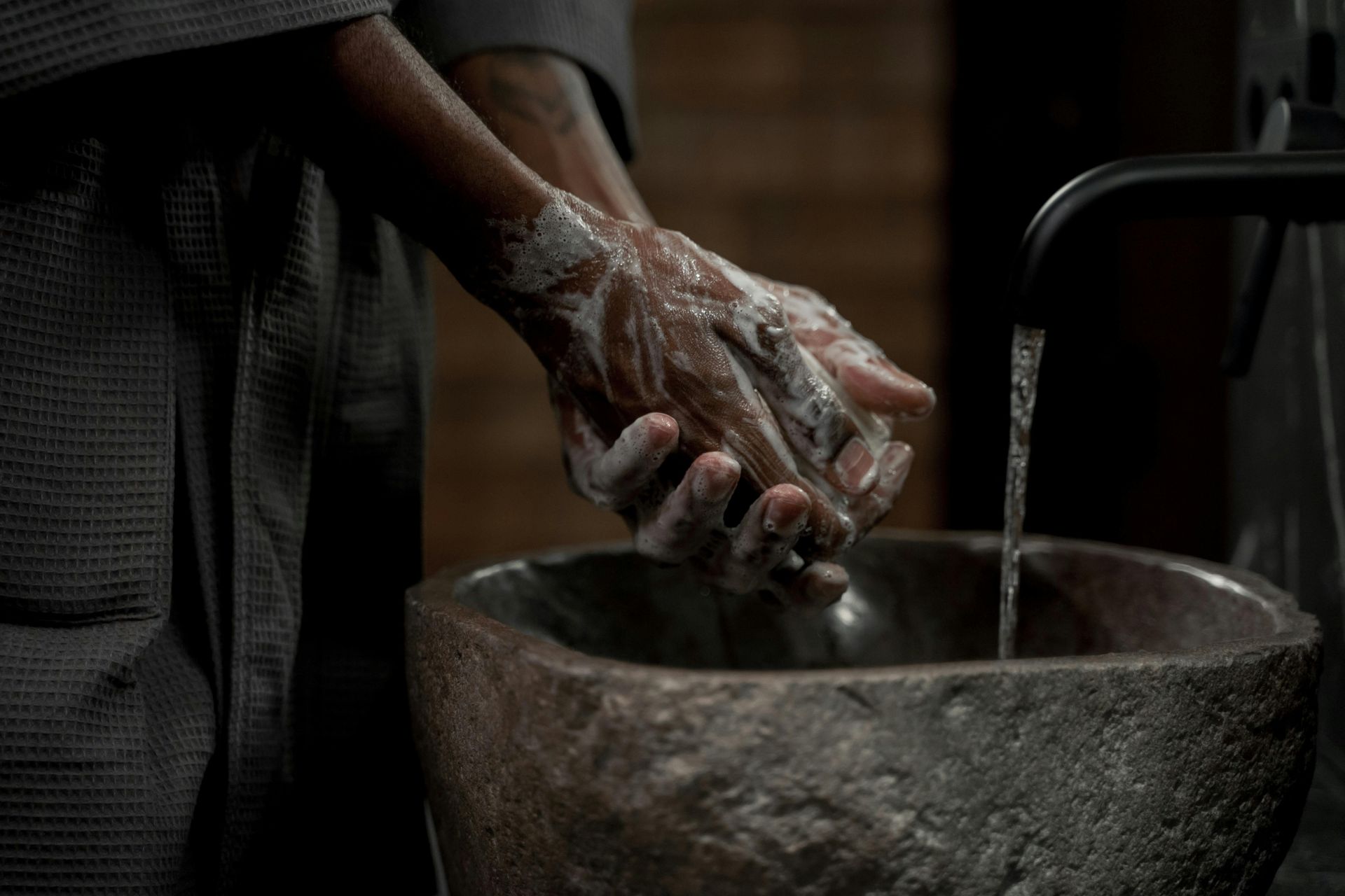 Un homme se lavant les mains avec du savon noir Les Bains de Marrakech sous l'eau courante dans un lavabo en pierre